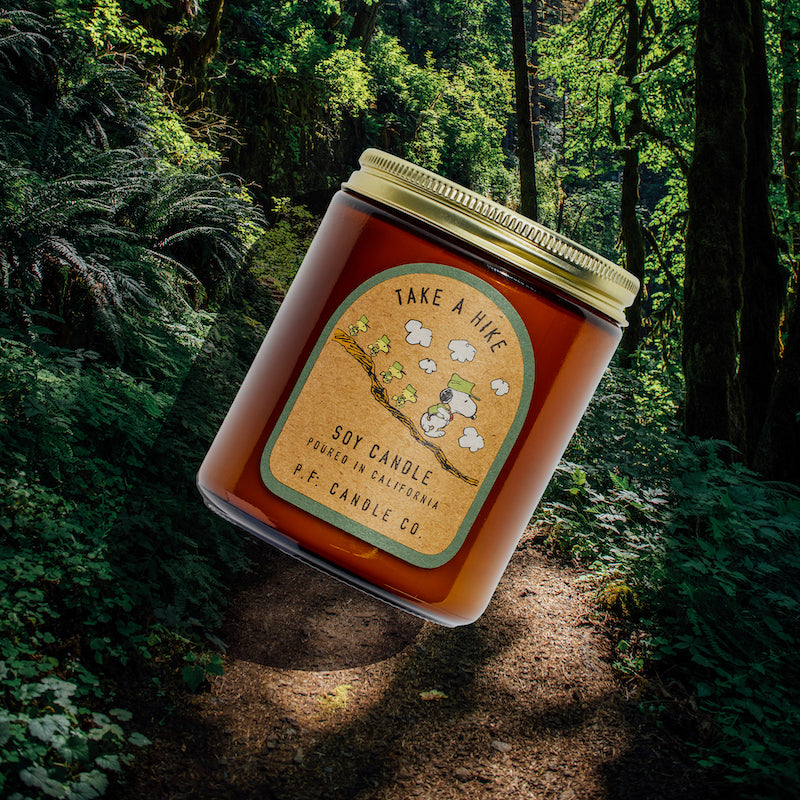 P.F. Candle Co. Take a Hike for Peanuts Standard Candle - Lifestyle - Inspired by inquisitive strolls along sun-soaked trails and bonding with buddies amongst towering trees, Take A Hike features aromatic, fresh notes of juniper shrub, pine cones, and tree sap to encourage moments of tranquility in any space.