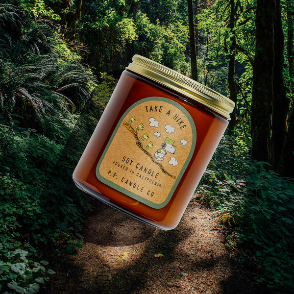 P.F. Candle Co. Take a Hike for Peanuts Standard Candle - Lifestyle - Inspired by inquisitive strolls along sun-soaked trails and bonding with buddies amongst towering trees, Take A Hike features aromatic, fresh notes of juniper shrub, pine cones, and tree sap to encourage moments of tranquility in any space.