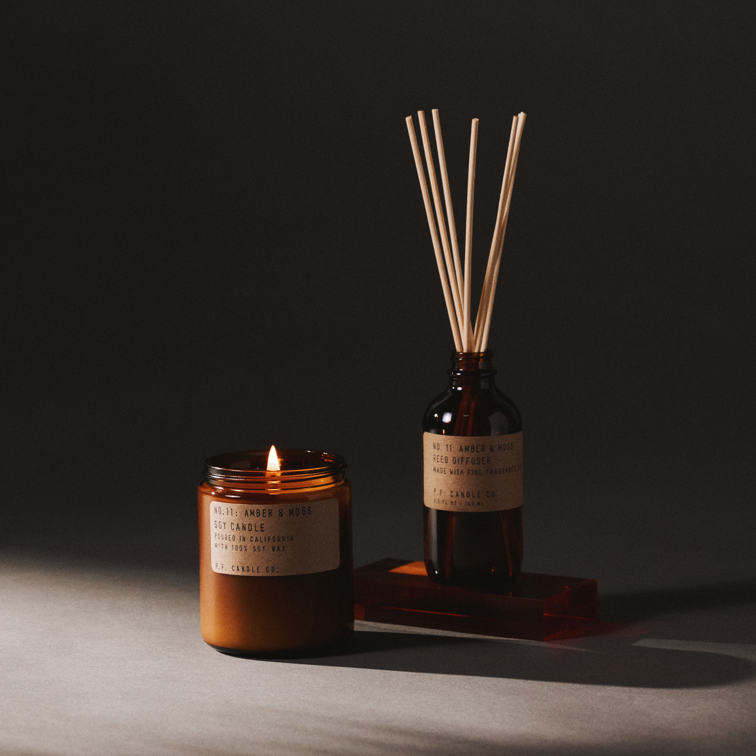 amber & moss candle and reed diffuser set on a dark background