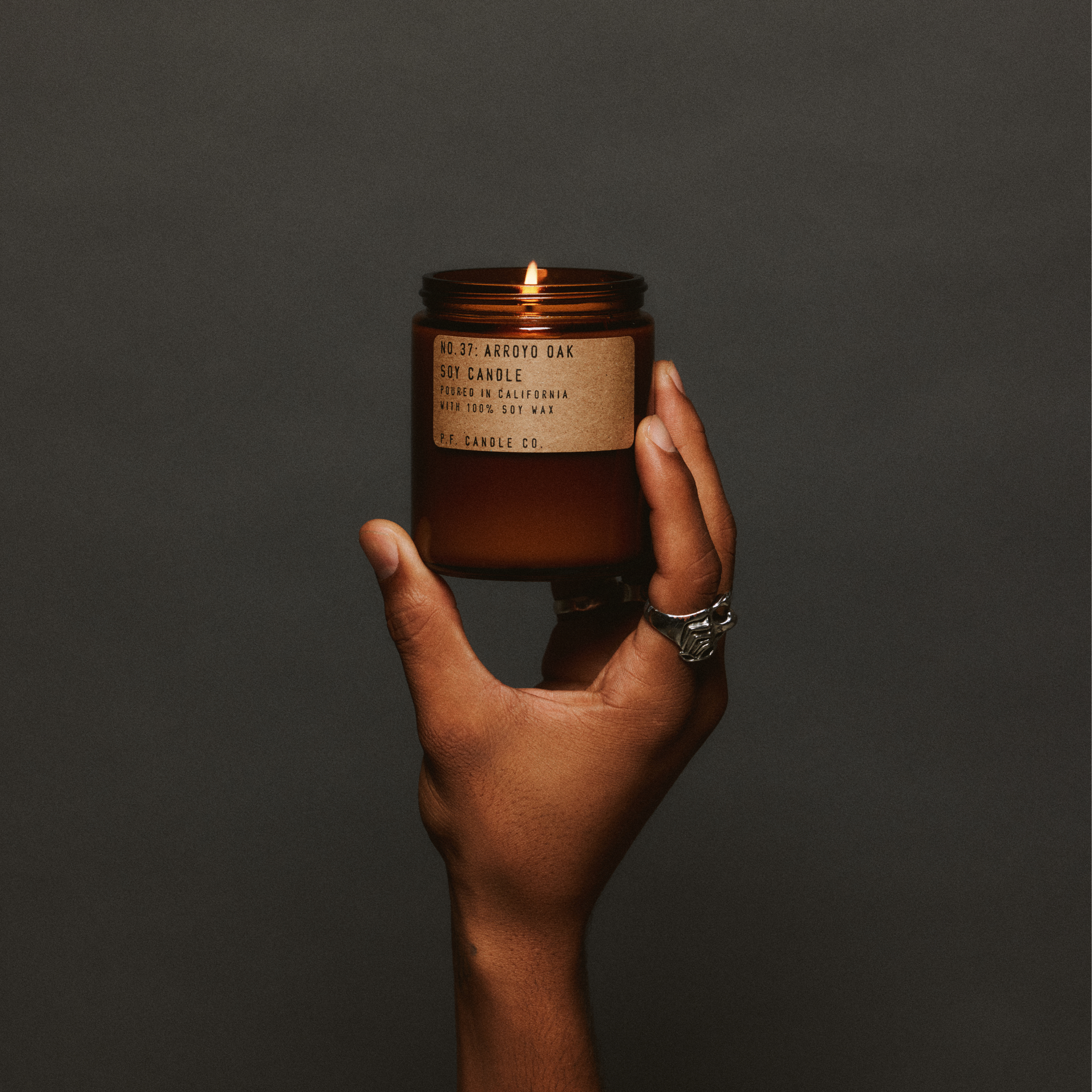 Hand holding a lit arroyo oak standard candle with a label against a dark background