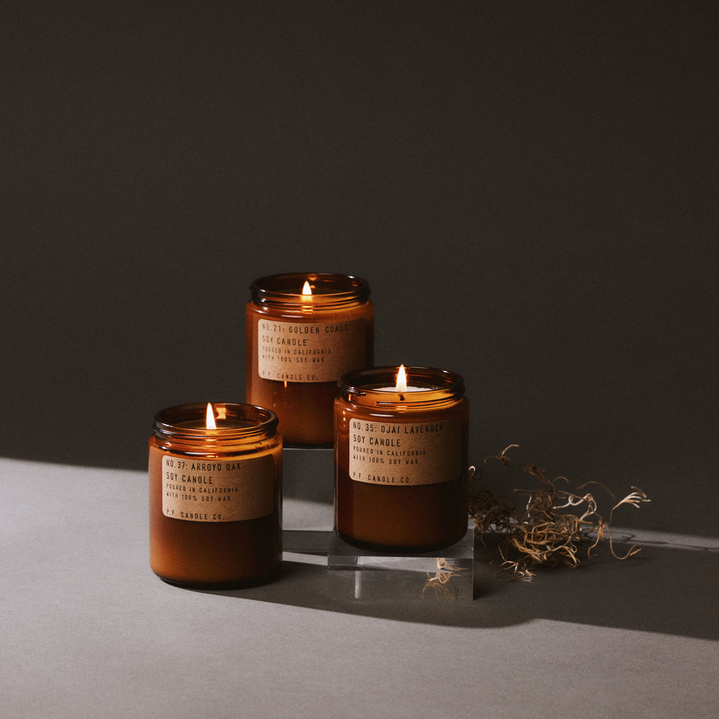 Three amber glass candles with labels on a dark surface