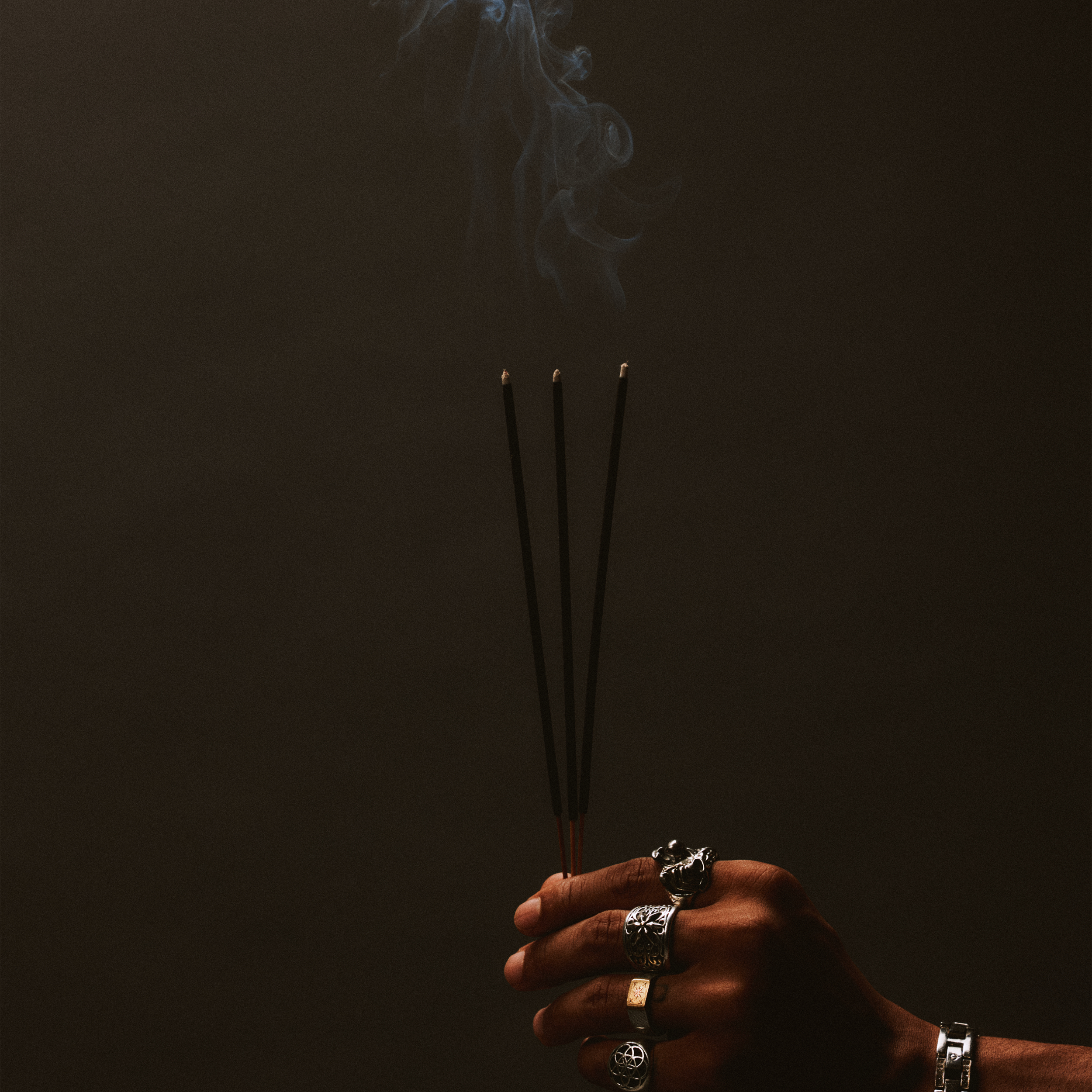 Hand holding charcoal incense sticks with smoke against a dark background