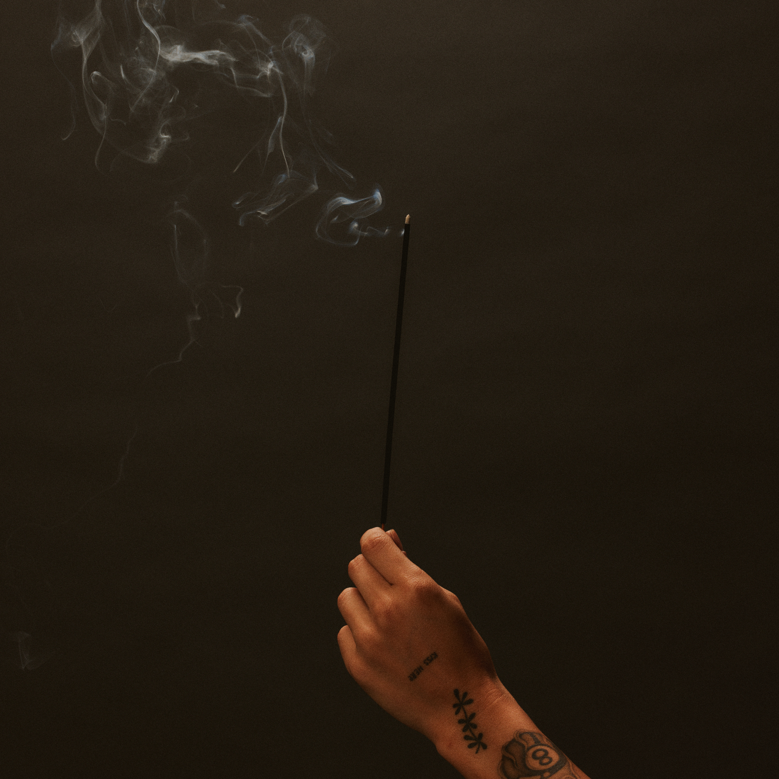 single incense stick with smoke in hand