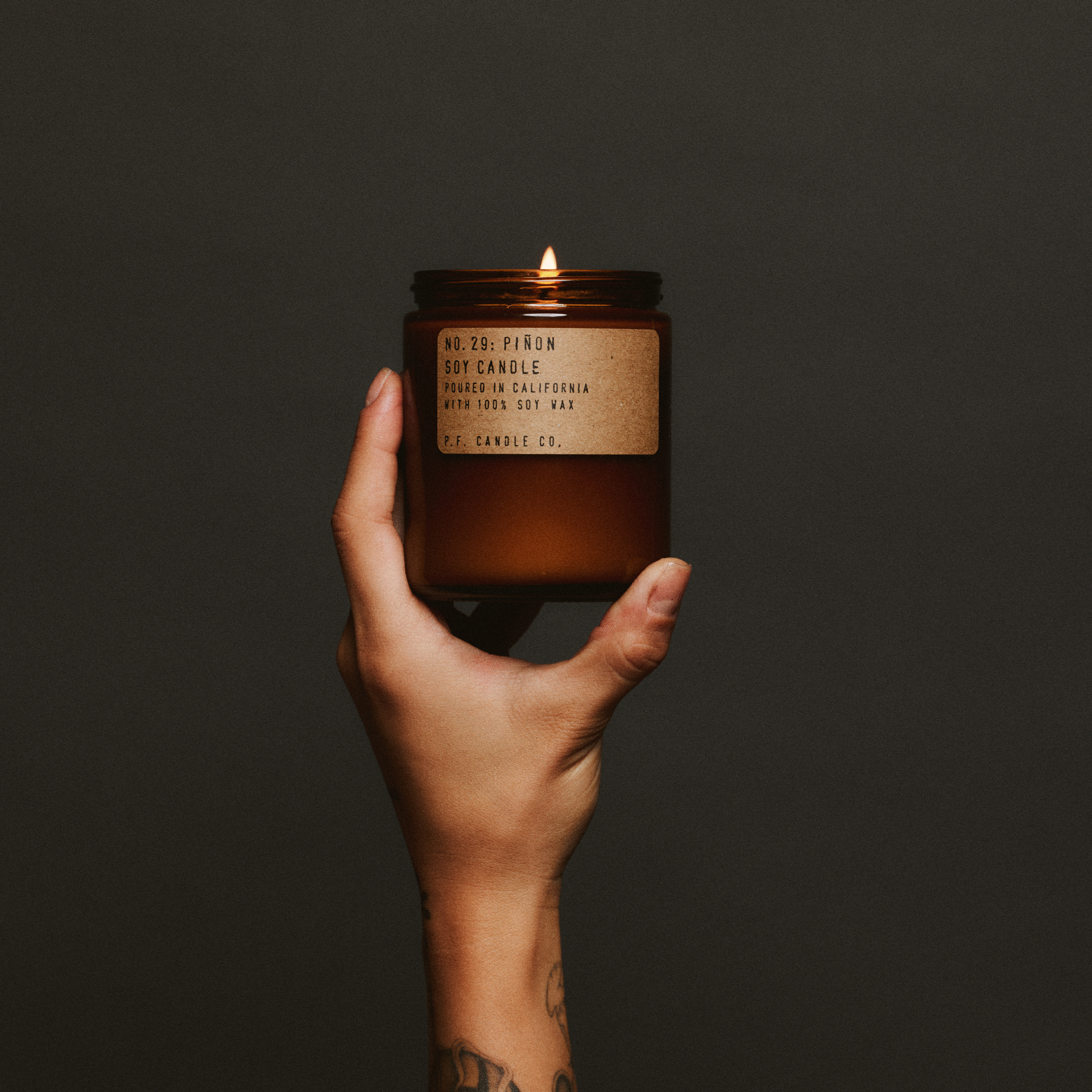 Hand holding a lit pinon standard candle with a label against a dark background