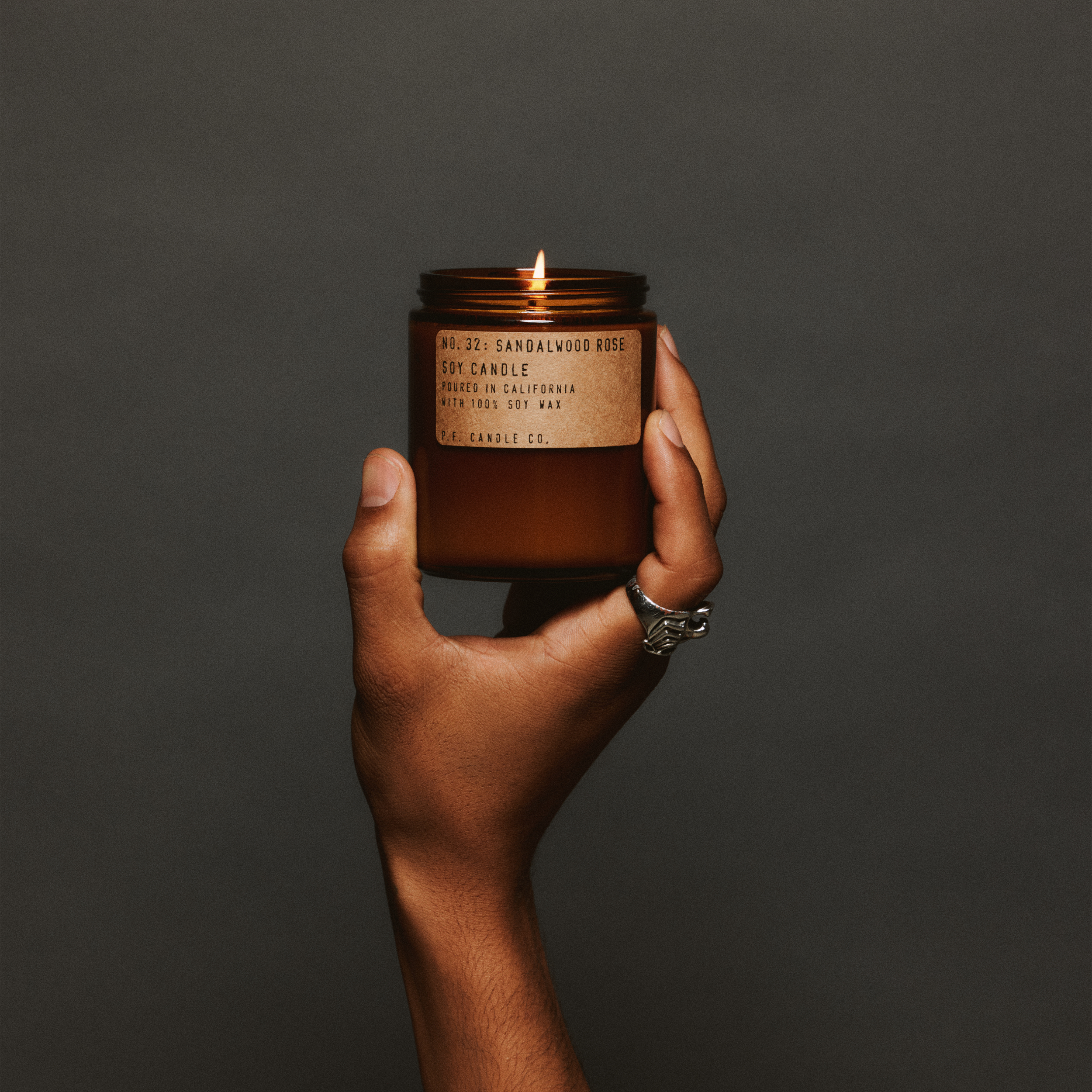 Hand holding a lit sandalwood rose standard candle with a label against a dark background